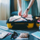 Woman packing suitcase for summer trip, including face masks and travel-sized antibacterial hand gels