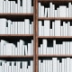 Image: White books stacked on bookshelves.