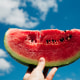 Slice of watermelon in hand over sky background