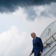 Image: President Joe Biden climbing down the stairs from a plane against a dark cloudy sky.