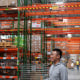 A young Asian man stands in front of shelves in a warehouse.
