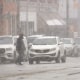 A person walks across a street amidst a snow storm.