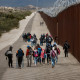 Asylum seekers walk along the U.S.-Mexico border barrier