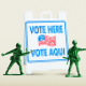 Photo illustration of green toy soldiers protecting a pixelated "Vote Here" street sign.