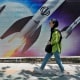 A woman walks past a banner showing missiles being launched, in Tehran on April 19, 2024.