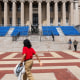 Three people walk on campus near the empty seats set up for commencement