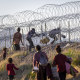 Migrants cross through a barbed-wire fence.