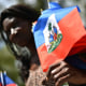 A woman sells Haitian national flags while looking at a group perform a dance during the celebration of Flag Day