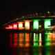 The Ringling Causeway bridge is illuminated by rainbow lights at night, reflecting over the water