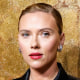 Scarlett Johansson stands for a portrait in front of a gold backdrop