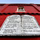 A stone table with the ten commandments listed on it, attached to the side of a red building exterior wall