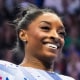 Simone Biles smiles with her arms extended by her sides