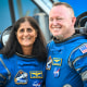 Suni William and Butch Wilmore stand and smile for a photo together in their Boeing space suits