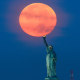 Full Harvest Moon Sets at Sunrise, the flame of the Statue of Liberty appears to touch the bottom of the moon in the sky