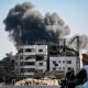 A man looks on from a vehicle as ahead smoke from Israeli bombardment rises above a destroyed building