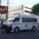 An ambulance vehicle drives on the street past buildings