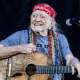 Willie Nelson holding a guitar while seated on stage