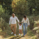 A dad, son, and mother hold hands and walk down a grassy path lined with bushes