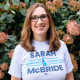 Sarah McBride stands in front of a bush with pink flowers and smiles