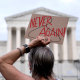 demonstrator holds a sign with a coat hanger, a symbol of the reproductive rights movement, with the words Never Again 