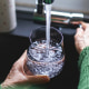 Close up of a senior woman's hand filling a glass of filtered water right from the tap in the kitchen sink at home