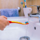 Detail of the arm of a girl in the bathroom, pouring water on her toothbrush in the sink.