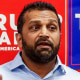 Kash Patel speaks, red and blue Trump Vance signs line the wall behind him