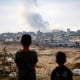 Young boys look at billowing smoke against a city skyline.