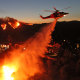 A helicopter drops water as the Palisades Fire grows