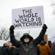 A man holds a sign saying "The whole world is watching"