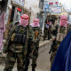Taliban fighters stand guard as a burqa-clad woman walks along a street
