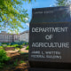 The sun flares over the top of the sign marking the headquarters building for the US Department of Agriculture.