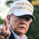 Donald Trump points and wears a white hat that says "Make America Great Again"