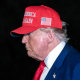 Donald Trump walks outside wearing a red MAGA hat, side profile