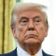 Inside an office President Donald Trump stands and holds a gold key in the air in front of a golden world cup trophy