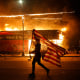 A protester carries a U.S. flag upside down as he walks past a burning building