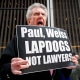 A protester holds a sign that reads, "Paul, Weiss Lapdogs not lawyers"