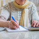 Old woman with calculator and notebook calculating gas and electricity bills.