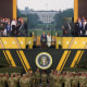 Image: A grandstand with attendees, including Trump and Melania, with soldiers and army tanks below it.