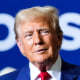 Donald Trump stands on stage in front of workers wearing safety vests
