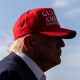 Donald Trump side profile, his face covered in shadow, wearing a red cap