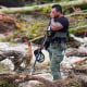 A person cover their face with their hand while standing in flood debris and fallen trees