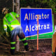 Two workers finish covering the Dade-Collier Training and Transition Airport sign with the "Alligator Alcatraz" sign
