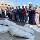 People pray over bodies covered in white body bags