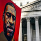 A poster of a painting of George Floyd is held up near a building exterior outside