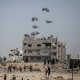 Parachutes fall near a partially destroyed building as people approach