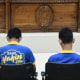 Two men, backs to camera, sit in front of a row of three judges in court