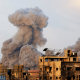 Palestinians stand as smoke rises following an Israeli strike, in Gaza City