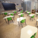 A classroom with desks, a large screen on the left wall, two fans can be seen