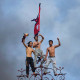 Three people stand on top of a building, the one in the center carries a Nepal flag
